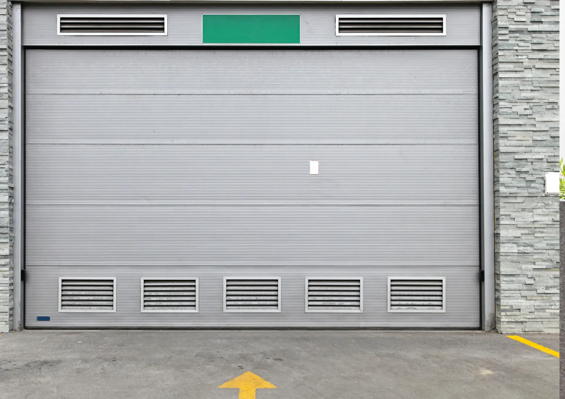 Porte de garage industrielle grise avec grilles d'aération sur un parking collectif