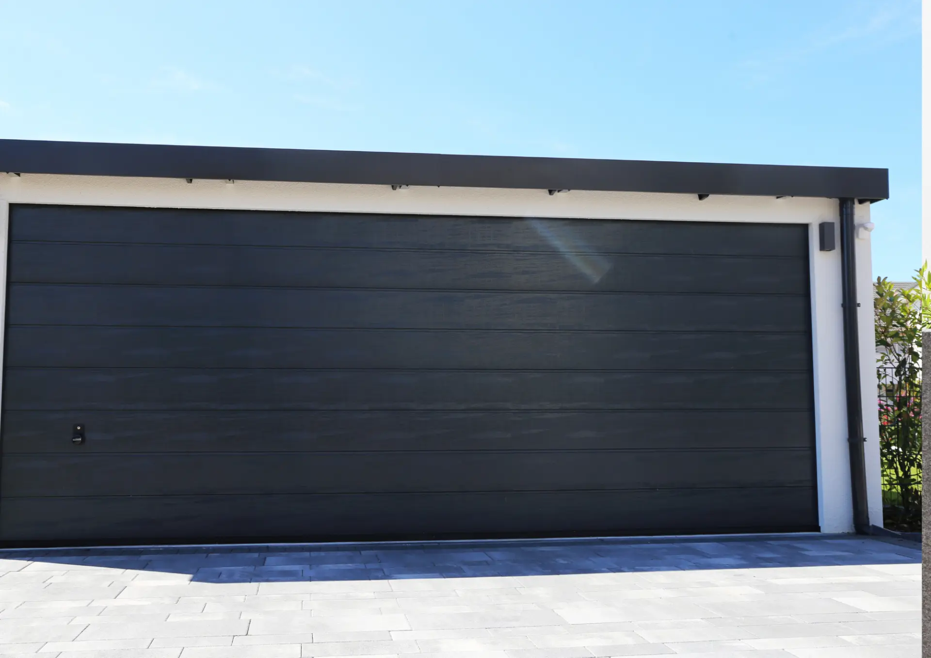 Grande porte de garage sectionnelle noire double sur un garage individuel