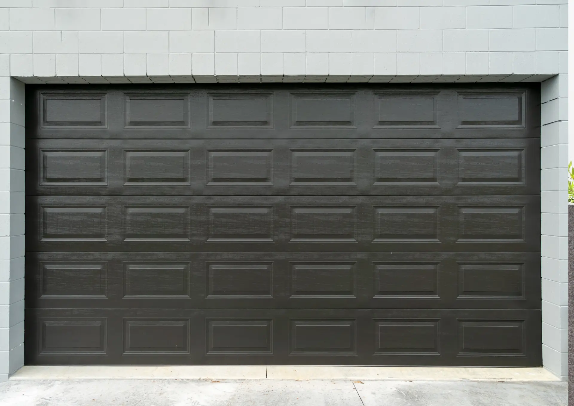 Porte de garage à cassettes noire posée dans un mur en parpaings peints