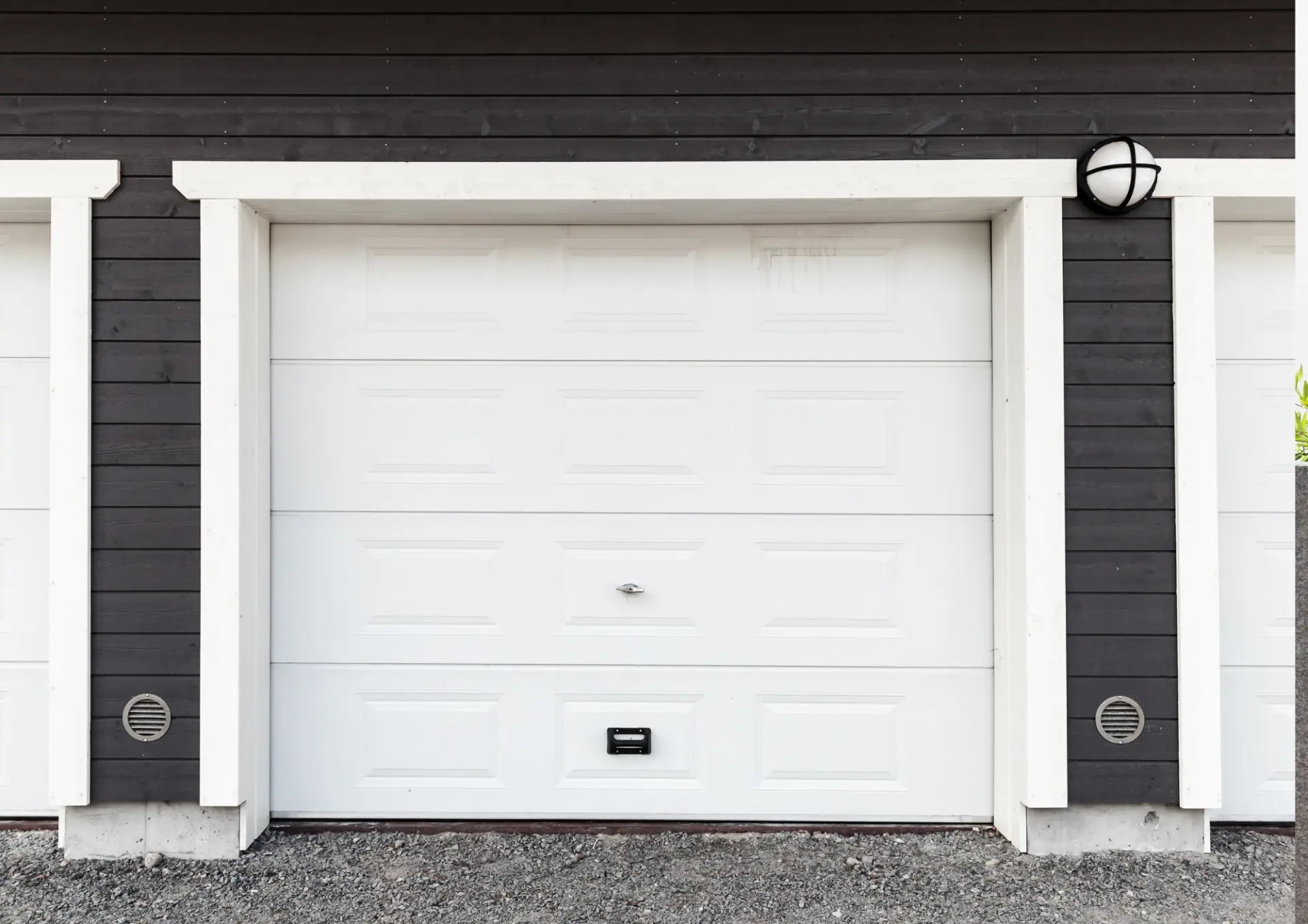 Porte de garage basculante blanche à cassettes sur un bâtiment bois foncé
